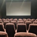 Photo of the cinema screen with rows of empty red fabric seats in front.