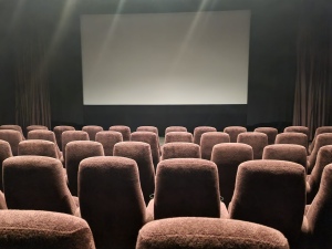 Photo of the cinema screen with rows of empty red fabric seats in front.