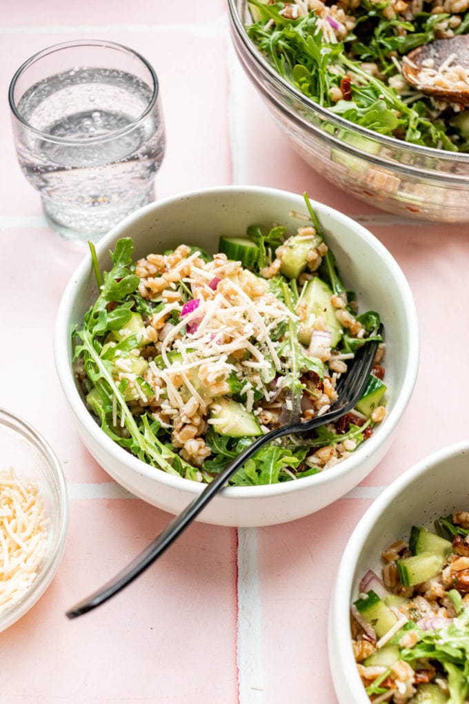 italian farro salad with arugula in white bowl with glass of water