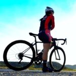 woman in cycling gear standing over bike with blue sky in the background