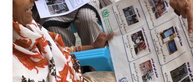 An elderly woman possibly from Pakistan seen looking at a poster and smiling.
