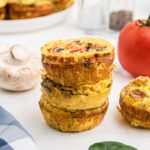 a stack of breakfast egg muffin cups with mushrooms and tomato in the background