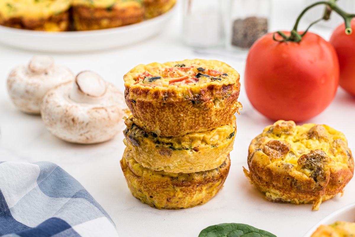a stack of breakfast egg muffin cups with mushrooms and tomato in the background