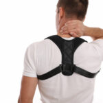 Man in white tee shirt wearing posture corrector harness and holding back of neck.
