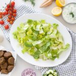 lettuce in a large bowl with falafel, cucumbers, tomatoes, dill, lemons