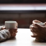 Close up woman and man holding cups of coffee on table