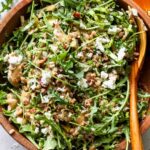 Arugula goat cheese salad tossed with honey mustard dressing in a wooden serving bowl