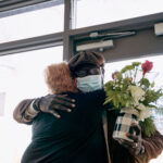 A man carrying a bouquet of flowers hugs a woman.