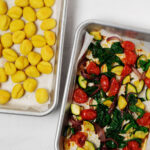 Two sheet pans have been covered with roasted vegetables and crispy gnocchi. They rest on a white surface.