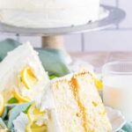 Slice of Lemon Layer Cake on white plate showing filling with whole cake in background on stand.