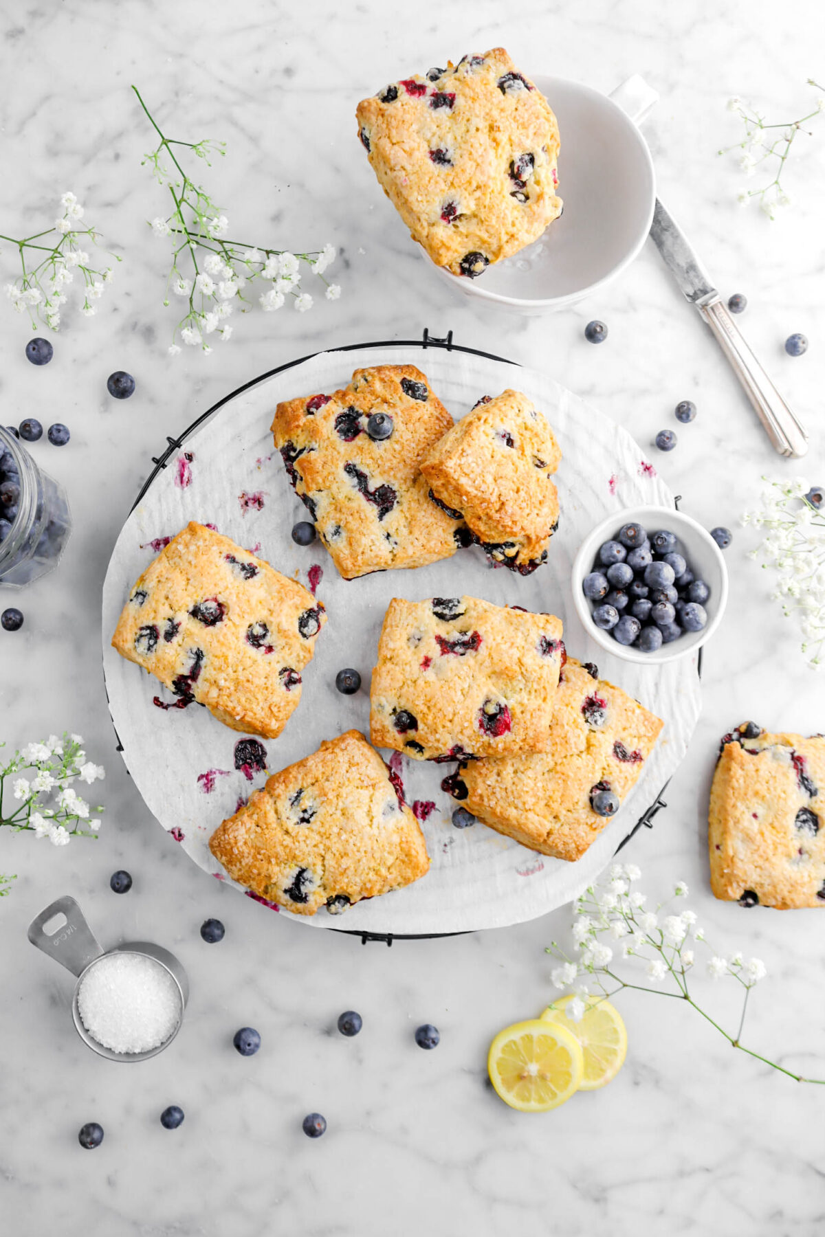 overhead shot of lemon blueberry scones on wire cooling rack with blueberries around, lemon slices, and flowers
