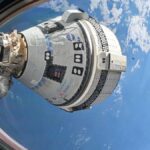 a white space capsule is seen through a spacecraft window, with earth in the background