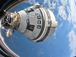 a white space capsule is seen through a spacecraft window, with earth in the background